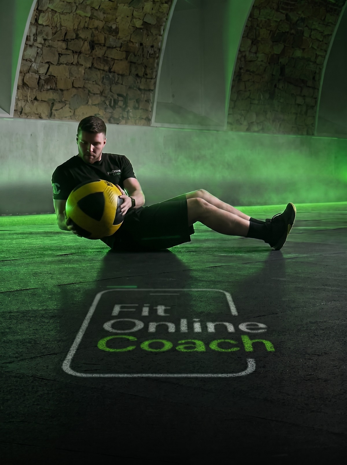 Tomek w russian twist z piłką lekarską; na podłodze sali logo FitOnlineCoach